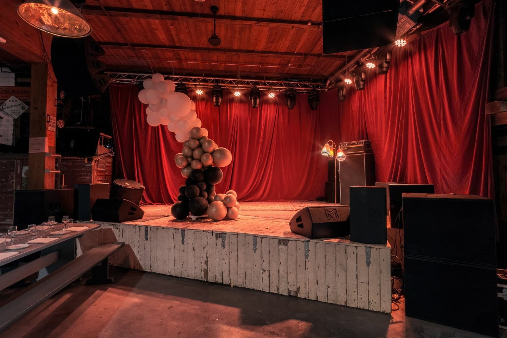 Hovedscenen i tømmerhallen med rødt sceneteppe i full bredde, lysrigg over og ballonginstallasjon på scenekanten.