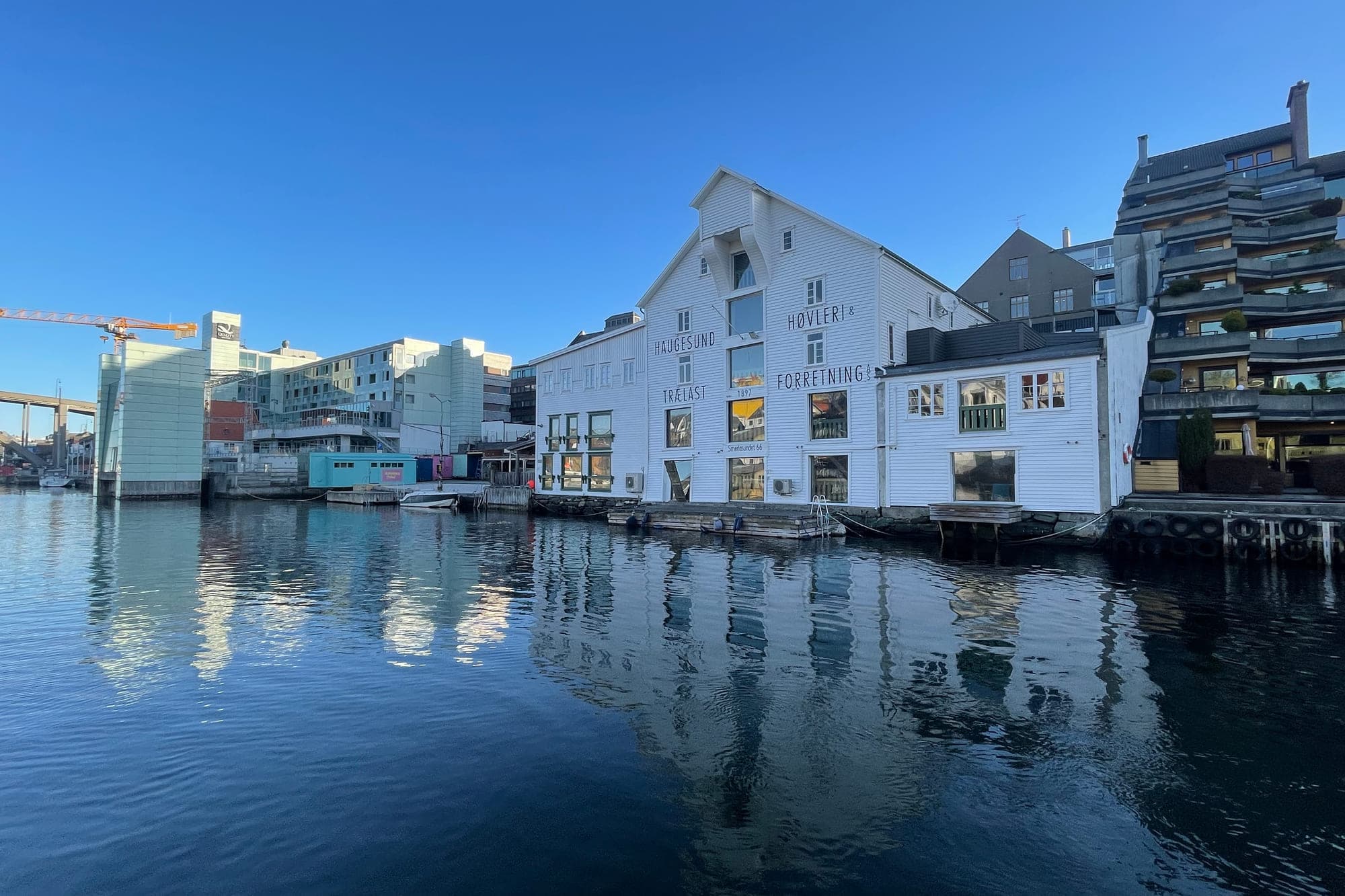 Høvleriet midt i Smedasundet en klar vinterdag, speilet i blikkstille vann, med badstua og bybebyggelsen langs kaien.