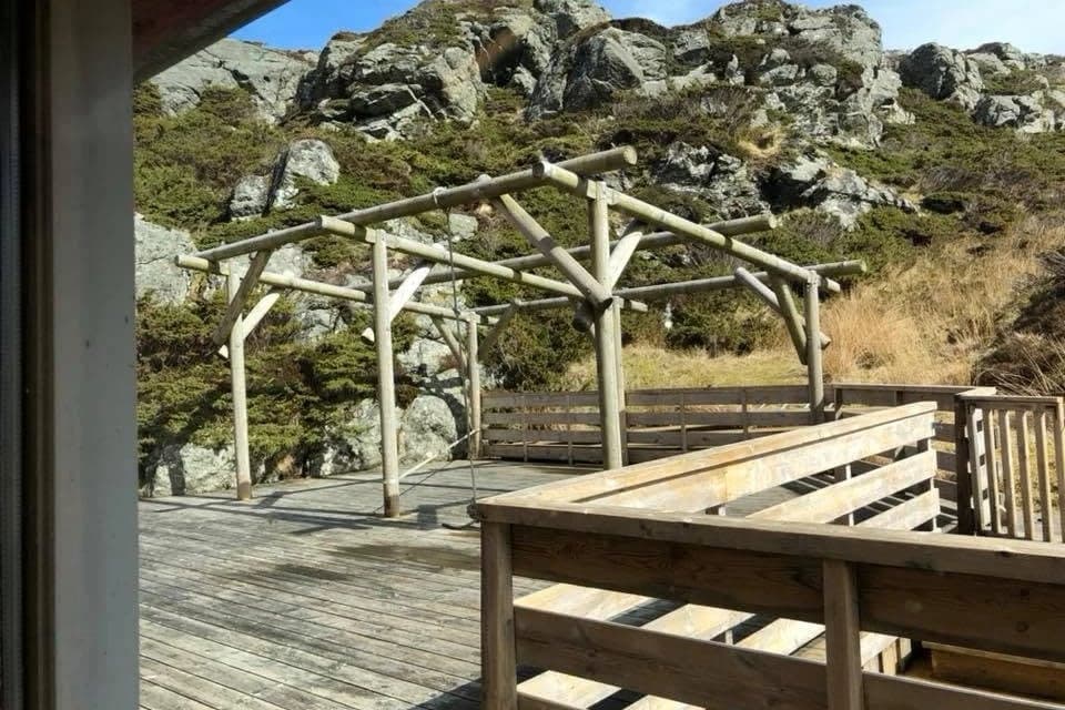Tredekket utenfor Vindkjeften med pergola i rundstokk, opp mot berget bak huset.