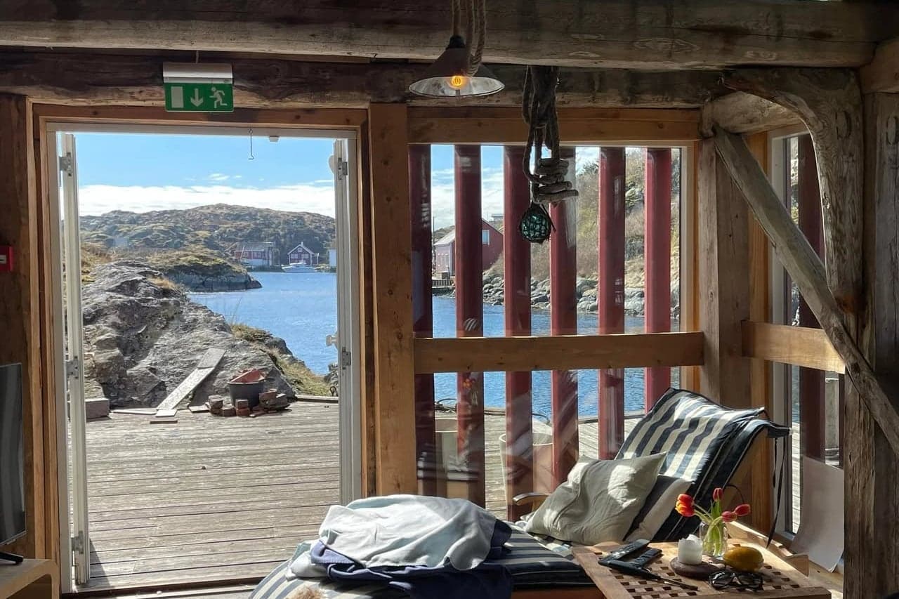 Åpen dør fra stua rett ut på kaia i Vindkjeften, med solseng, tulipaner på bordet og sjøen utenfor.